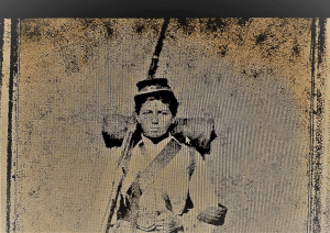 A imagem mostra Jovita Feitosa em uniforme militar à época, 1865, usa na cabeça um gorro (chapéu) militar, carrega no ombro direito uma arma de cano longo, aparentando ser um fuzil. Conduz na cintura uma cartucheira e uma faca. Nas costas leva uma manta enrolada no formato de charuto.