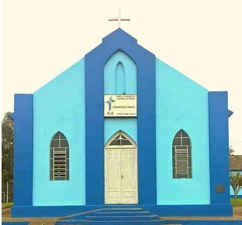 Imagem de uma capela pitada com dois tons fortes de azul, um mais claro e outro mais escuro. A capela possui duas janelas e, em seu centro, uma porta branca. Acima da porta há uma placa
