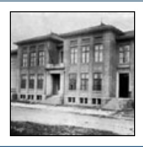 A imagem está em preto e branco, caracteriza uma escola com um prédio de dois andares divididos por blocos com diversas janelas antigas e portais com escadas, além do subsolo e uma estrada de terra na frente.