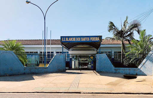 Na imagem, aparece a fachada principal da escola Estadual Blanche dos Santos Pereira, com suas paredes externas pintadas de azul, coqueiros em seus jardins, e um amplo calçamento na frente do edifício. 
