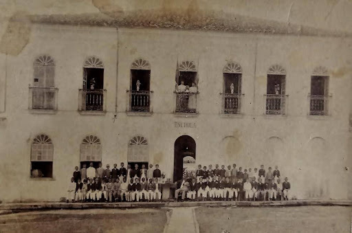 Fachada antiga do Internato e Externato Sant'Anna. Aparecem pessoas posando para a fotografia na frente do prédio, com janelas e sacadas coloniais. A fotografia está em preto e branco.